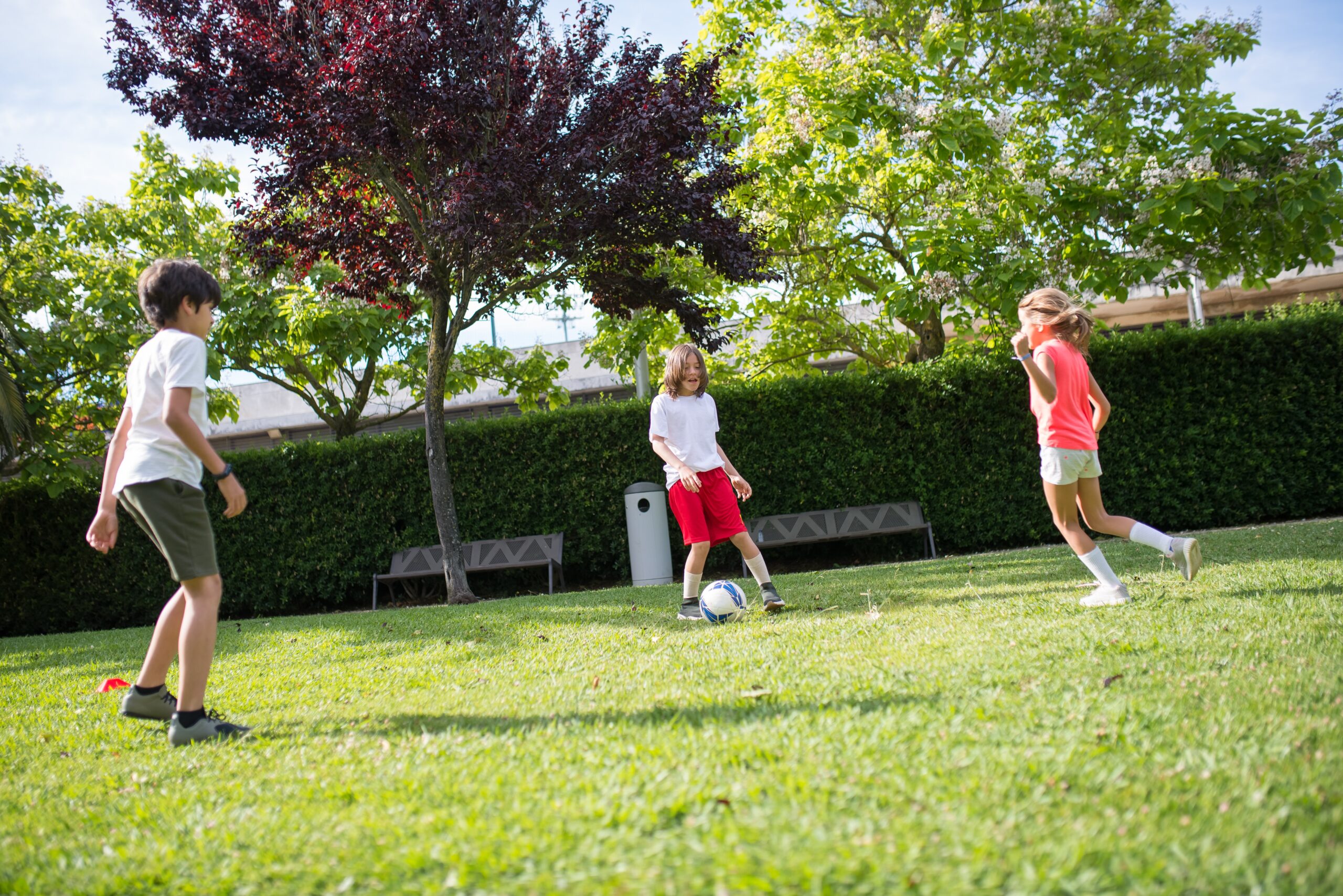 Bilden visar barn som spelar fotboll. Bland uteleksaker finns fotbollsmål, studmattor och springcyklar samt trampbilar som skapar roliga utelekar året om